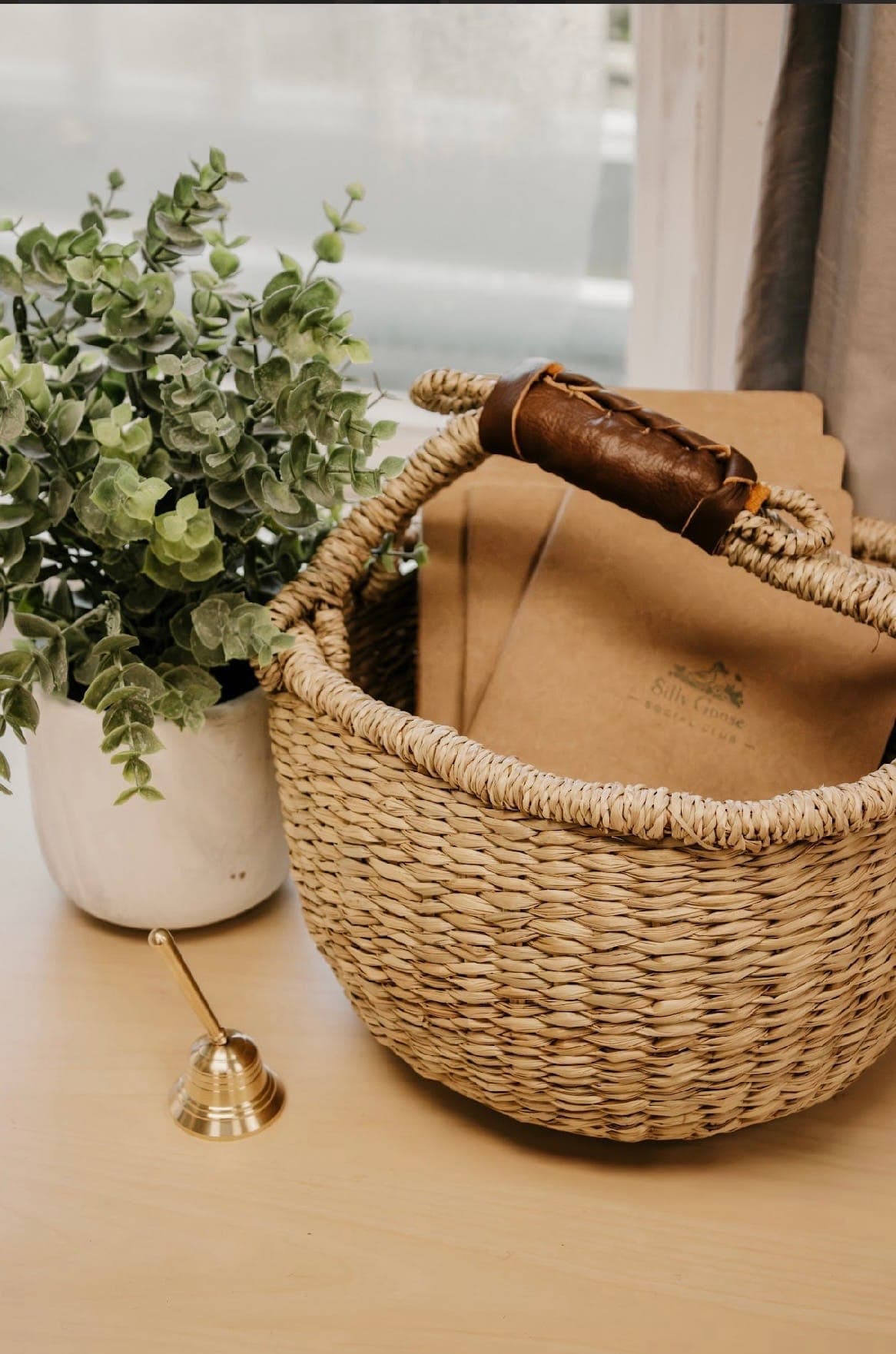 A woven basket of Silly Goose Social Club journals beside the storytime bell